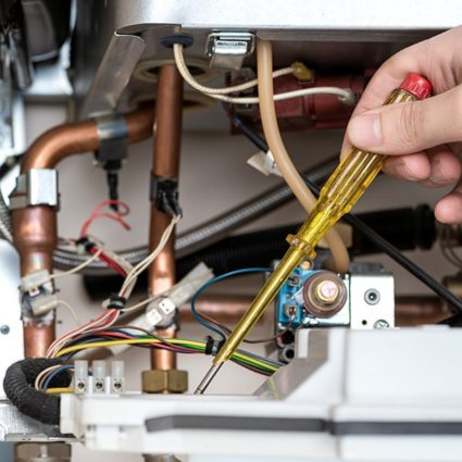 A Duffett technician uses a screwdriver to fix an internal component during a tankless water heater repair project.